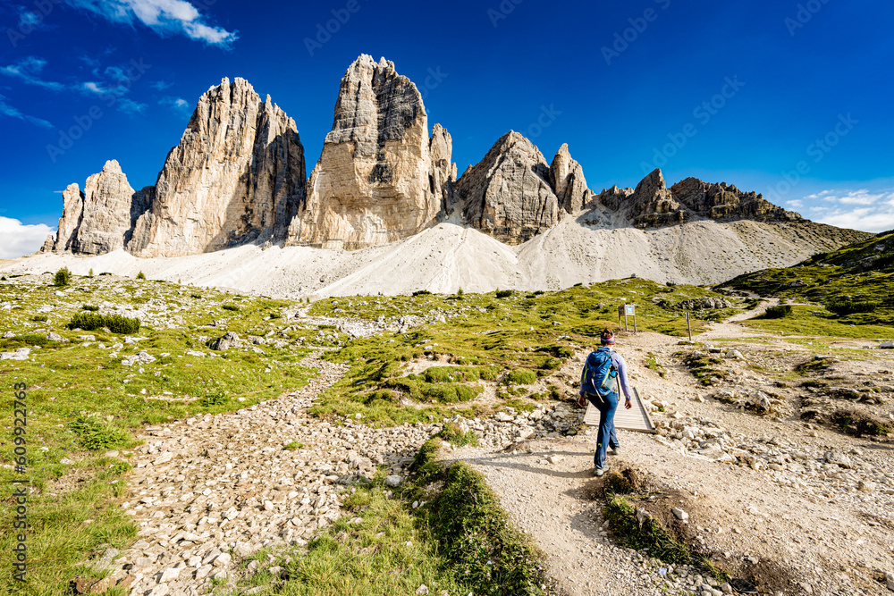 Young woman walks on hike trail with scenic view on Tre Cime in the afternoon. Tre Cime, Dolomites, South Tirol, Italy, Europe.