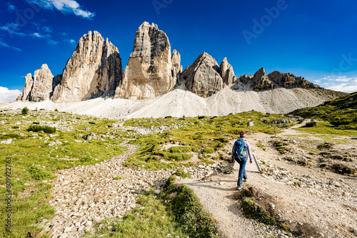 Young woman walks on hike trail with scenic view on Tre Cime in the afternoon. Tre Cime, Dolomites, South Tirol, Italy, Europe. © Michael