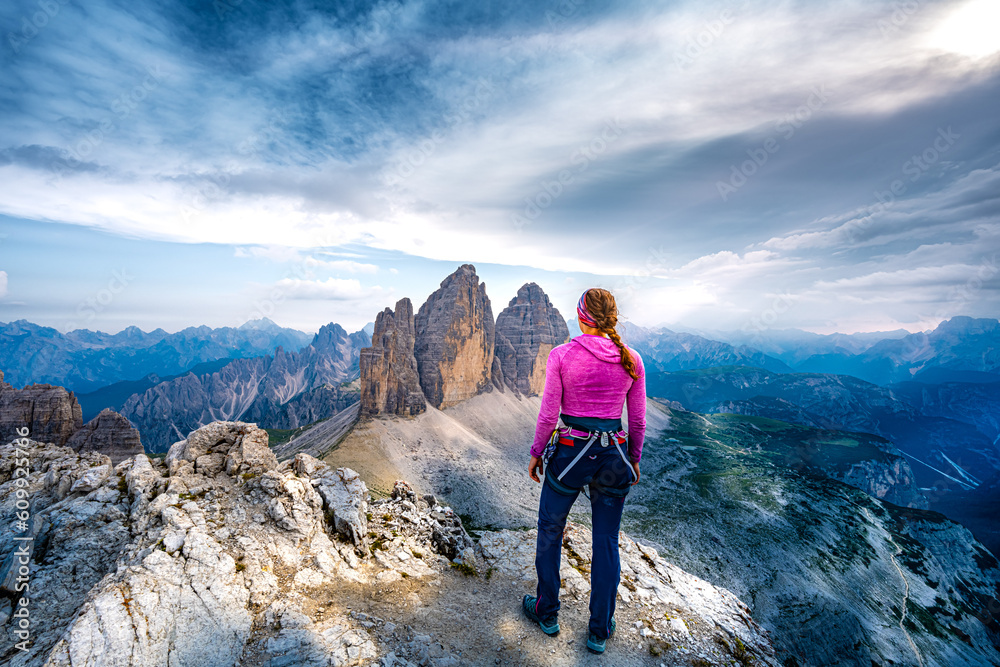 Fototapeta premium Young athletic woman enjoys summit view on Tre Cime from Paternkofel in the evening. Tre Cime, Dolomites, South Tirol, Italy, Europe.