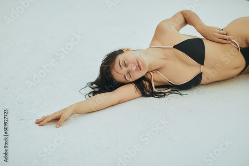 alluring woman in black bikini, sexy model with wet hair posing in luxury resort, Miami, Florida, USA, blurred background, laying down on white surface, poolside relaxation