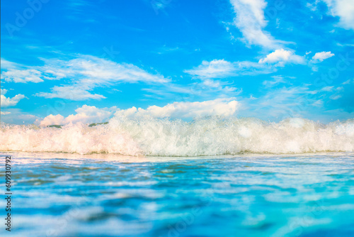 Close-up of the sea wave with the foam surging on the shore. View of sea water in soft focus. Background in a light blur on the theme of a serene summer vacation and relaxed vacation.