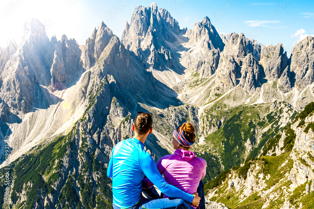 Sitting young couple enjoys epic view on Cadini di Misurina mountain range in the morning. Tre Cime, Dolomites, South Tirol, Italy, Europe.
