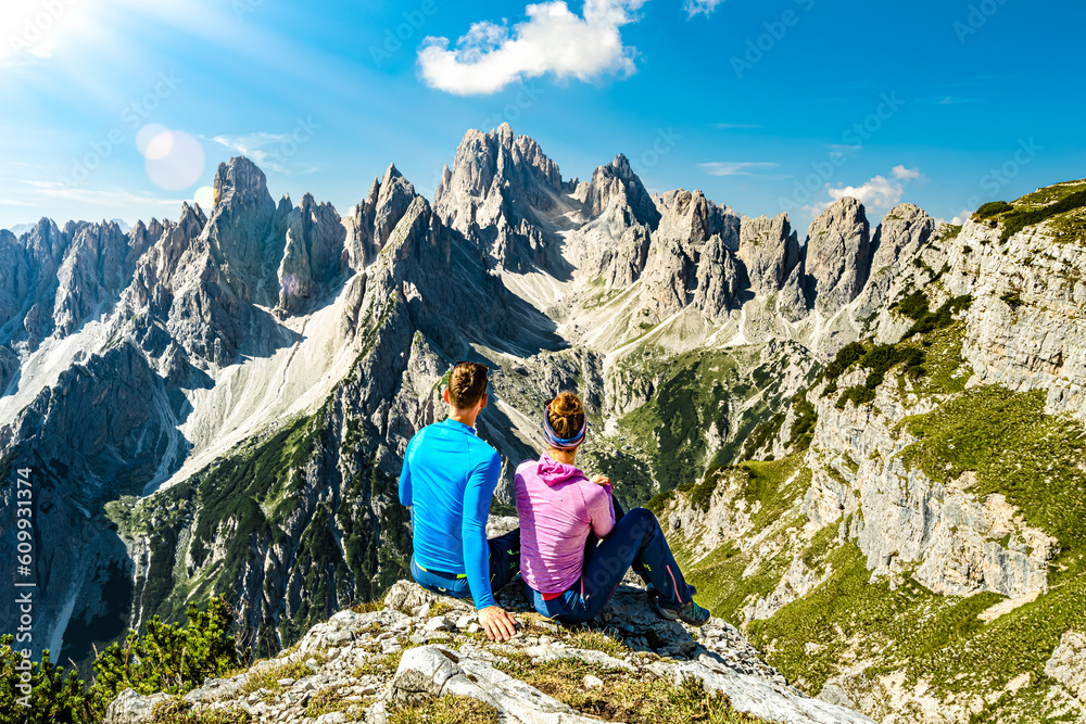 Sitting young couple enjoys epic view on Cadini di Misurina mountain range in the morning. Tre Cime, Dolomites, South Tirol, Italy, Europe. Sitting young couple enjoys epic view on Cadini di Misurina mountain range in the morning. Tre Cime, Dolomites, South Tirol, Italy, Europe.