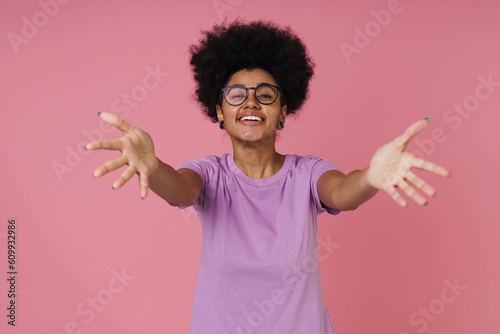 Friendly african woman stretching her arms for hug while standing isolated over pink wall