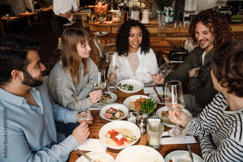 Group of cheerful friends talking and drinking wine while dining in restaurant