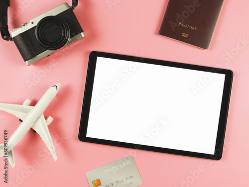 flat lay of digital tablet with blank white screen, airplane model, passport, credit card and digital camera isolated on pink background. travel planning concept.