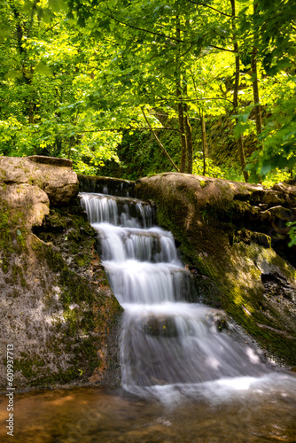 Small artificial waterfallcascade in romantic natural reserve “Hönnetal“ – Hoenne river canyon, Sauerland Germany. Sunny idyllic atmosphere on hiking trail from Hemer to Balve called “Waldroute“.