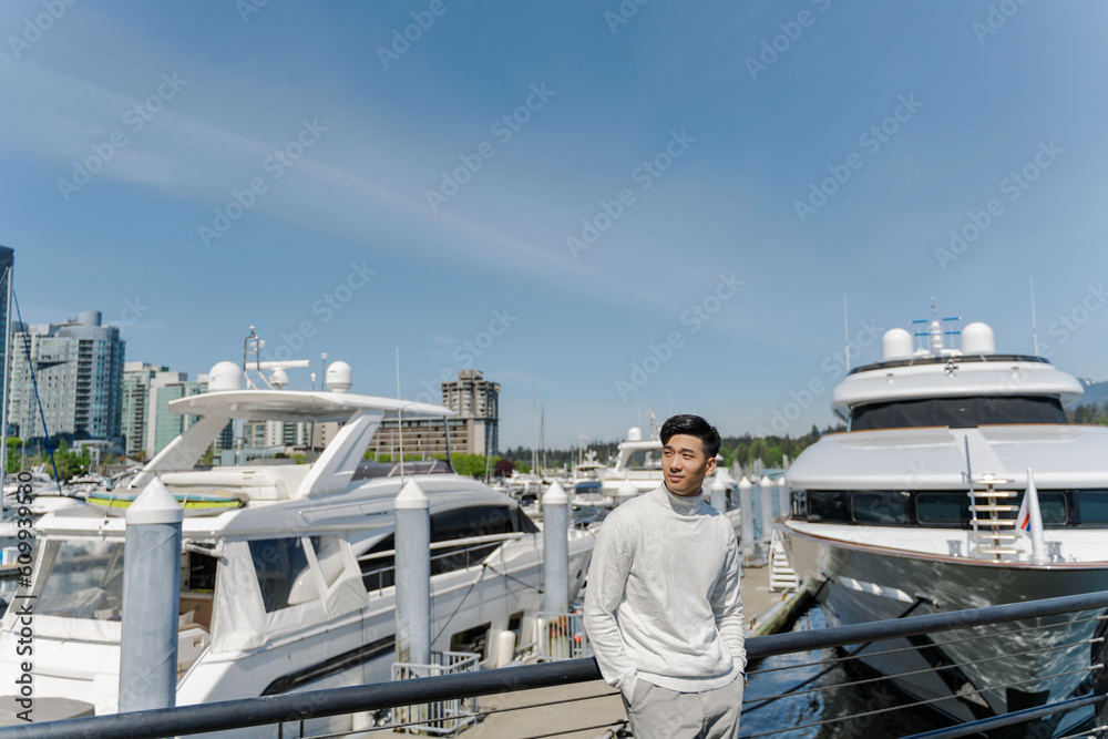 Portrait of asian rich man standing near expensive yachts, looking away outdoors