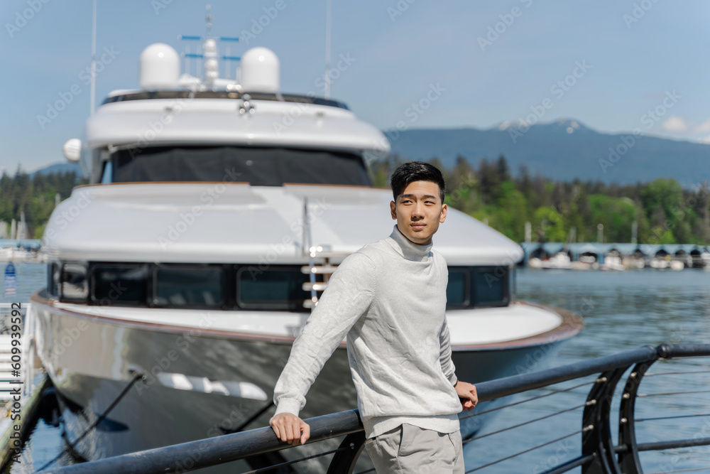 Handsome asian businessman standing near yacht, looking away. Attractive chinese businessman