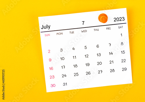 The July 2023 and wooden push pin on yellow background.