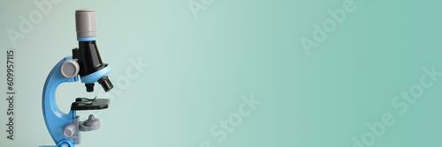 Children's toy microscope on a light blue background. An exact copy of a professional microscope with illumination for the stage during the study. Banner with free space for text