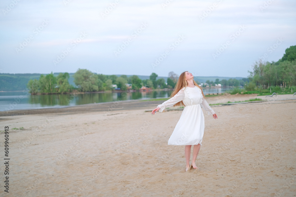 Beautiful redheaded girl on the beach in summer running on the sand in a white dress. Beautiful redheaded girl on the beach in summer running on the sand in a white dress.