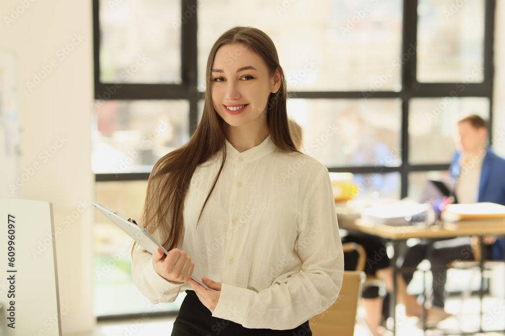 Smiling woman in white blouse holds clipboard in office Smiling woman in white blouse holds clipboard in office