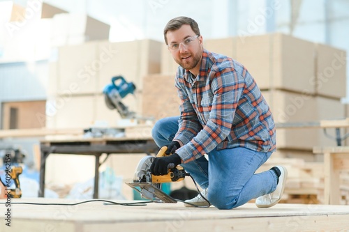 A carpenter works on woodworking the machine tool. Man collects furniture boxes. Saws furniture details with a circular saw. Process of sawing parts in parts. Against the background of the workshop.