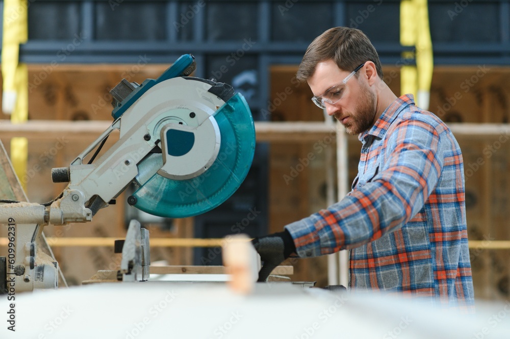 A carpenter works on woodworking the machine tool. Man collects furniture boxes. Saws furniture details with a circular saw. Process of sawing parts in parts. Against the background of the workshop. A carpenter works on woodworking the machine tool. Man collects furniture boxes. Saws furniture details with a circular saw. Process of sawing parts in parts. Against the background of the workshop.