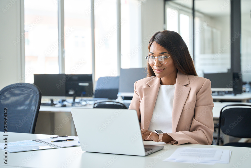Professional business woman employee working on computer in office. Young busy African American female company finance manager executive using laptop managing financial project sitting at desk. Professional business woman employee working on computer in office. Young busy African American female company finance manager executive using laptop managing financial project sitting at desk.