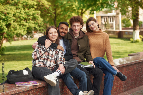 Sitting and smiling. Four young students in casual clothes are together outdoors
