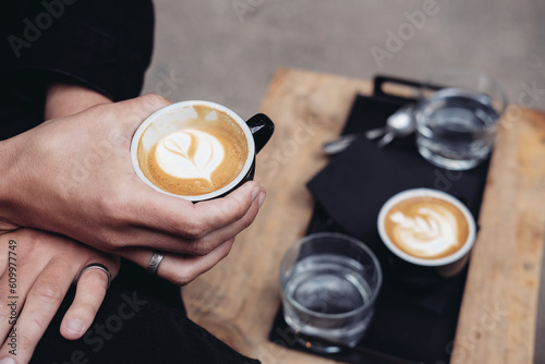 Man holding a cup of cappuccino. A flat white coffee on a wooden table outside 