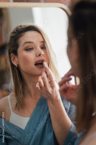 Young woman doing her make-up  looking in mirror.