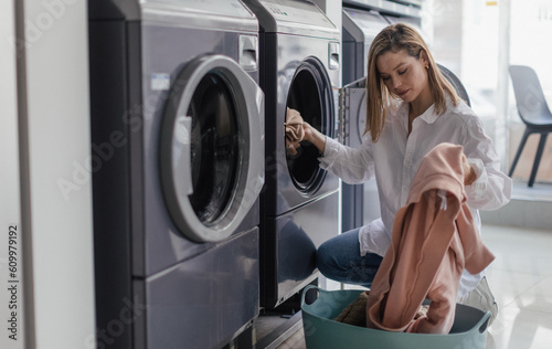 Slika na platnu Young woman loading washing machine in public laundry.