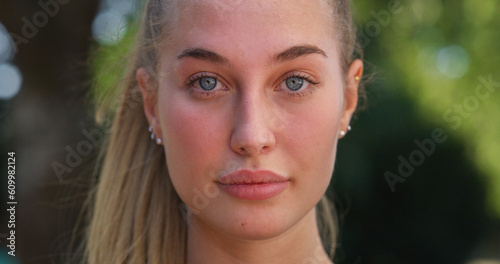 Close Up Portrait of Beautiful Young Woman Looking at Camera Neuterally with a Greenery Background. Blond Female Teenager Enjoying Fresh Air in the Park and Taking Care of her Wellbeing © Kitreel