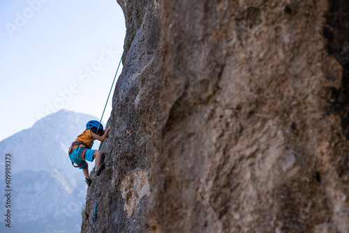 Children's rock climbing. The boy climbs a rock against the backdrop of mountains. Extreme hobby. An athletic child trains to be strong.