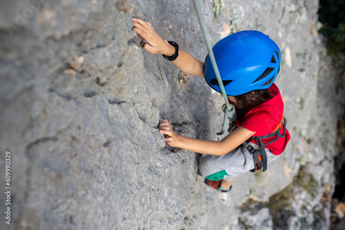 child rock climber in a blue protective helmet overcomes the route in the mountains. children's sports in nature.