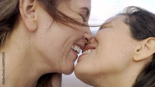 Gay lesbian couple kissing with beach on background during summer travel vacations