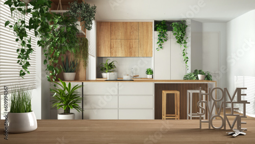 Wooden table, desk or shelf with potted grass plant, house keys and 3D letters home sweet home, over white kitchen with island, architecture interior design, urban jungle