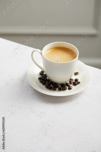Cup of coffee and beans, on white marble table