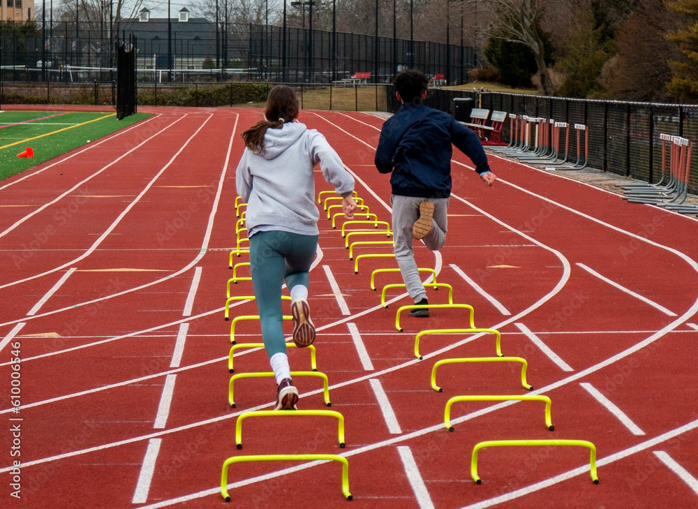 Fototapeta premium Two runners running over six inch mini hurdles on a track