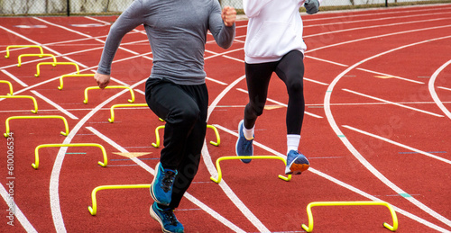 Two runners running over small yellow hurdles in lane on a track