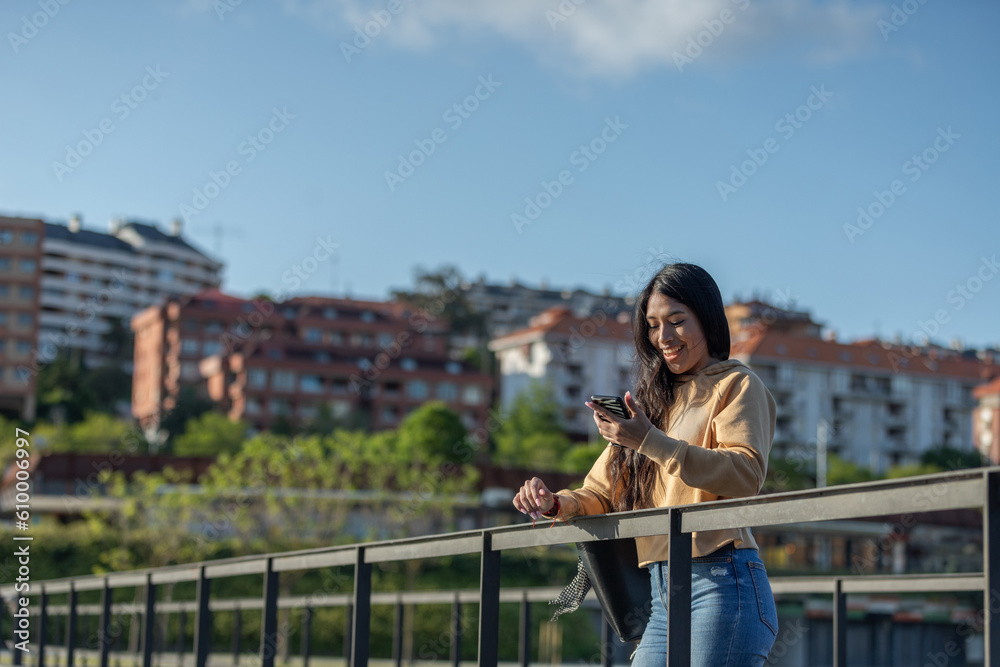 Happy woman walking and writing or reading sms messages online on a smartphone while the wind moves her hair on a street