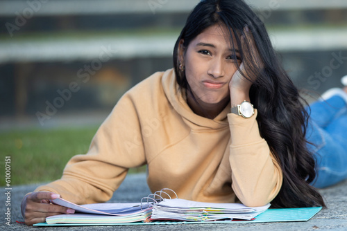 overwhelmed young woman studying outside college or high school campus with her notes in blue folder