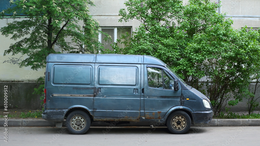 An old rusty minibus is parked against the wall of a house, Dybenko Street, St. Petersburg, Russia, May 2023
