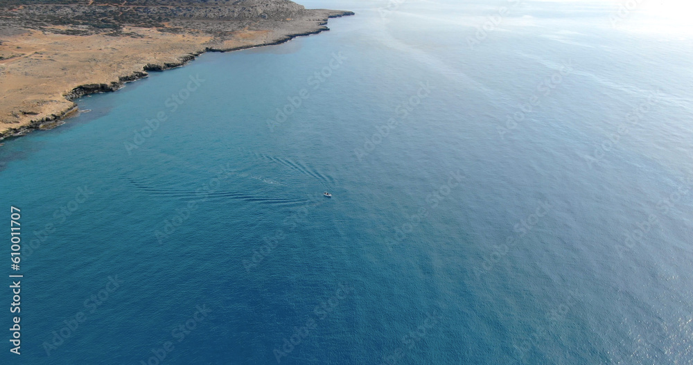 The copter flight over the steep shore of island and the deep blue sea and a small yacht or boat sailing on water in Cyprus.