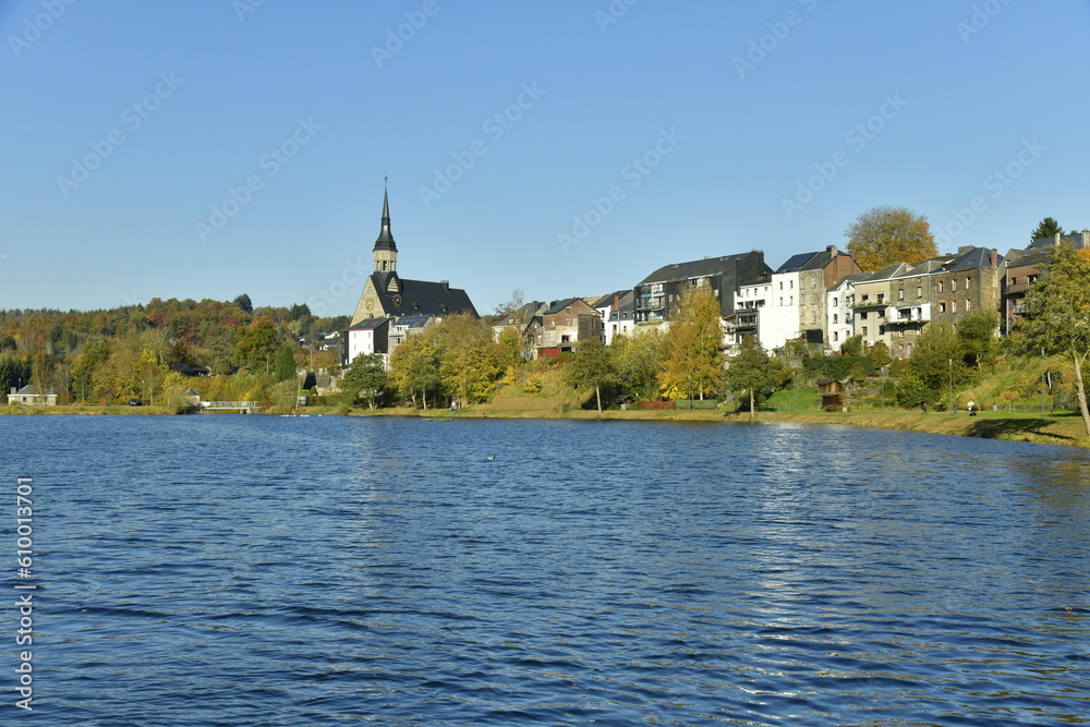 Le village de Vielsalm et l'eglise paroissiale Saint Gengoux dans un paysage champêtre le long du lac des Doyards sous un ciel clair d'automne