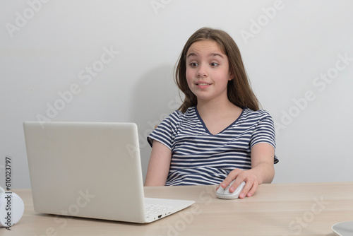 A teenage girl with a computer at the table is pleasantly surprised by an incoming message.