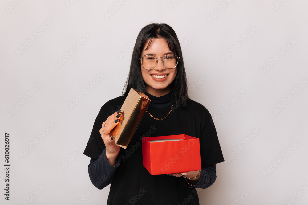 Cheerful woman is holding an opened red gift box while smiling at the camera. Cheerful woman is holding an opened red gift box while smiling at the camera.