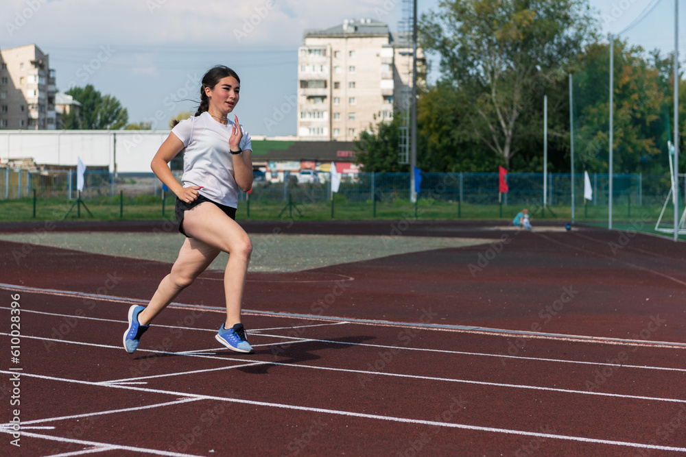 Young girl running on the running track at the stadium outdoors