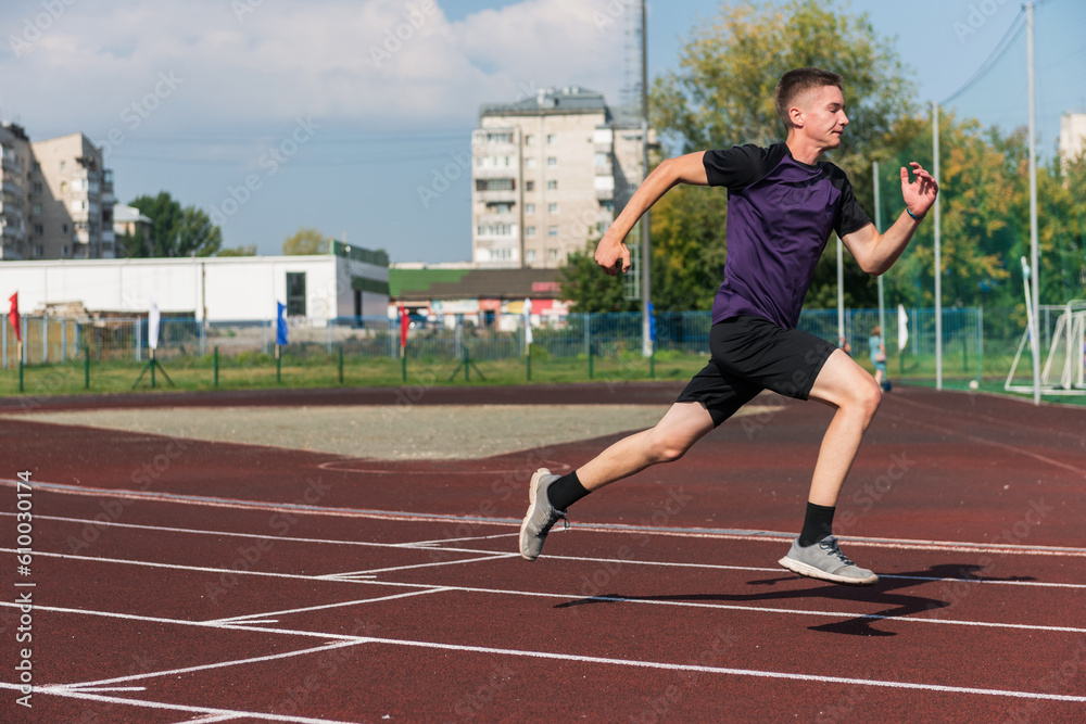 Obraz premium Young teen boy running on the running track at the stadium outdoors