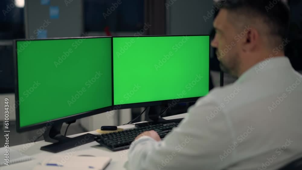 Man Uses Desktop Computer With Two Green Screen Mock Ups Working at Office Man Uses Desktop Computer With Two Green Screen Mock Ups Working at Office