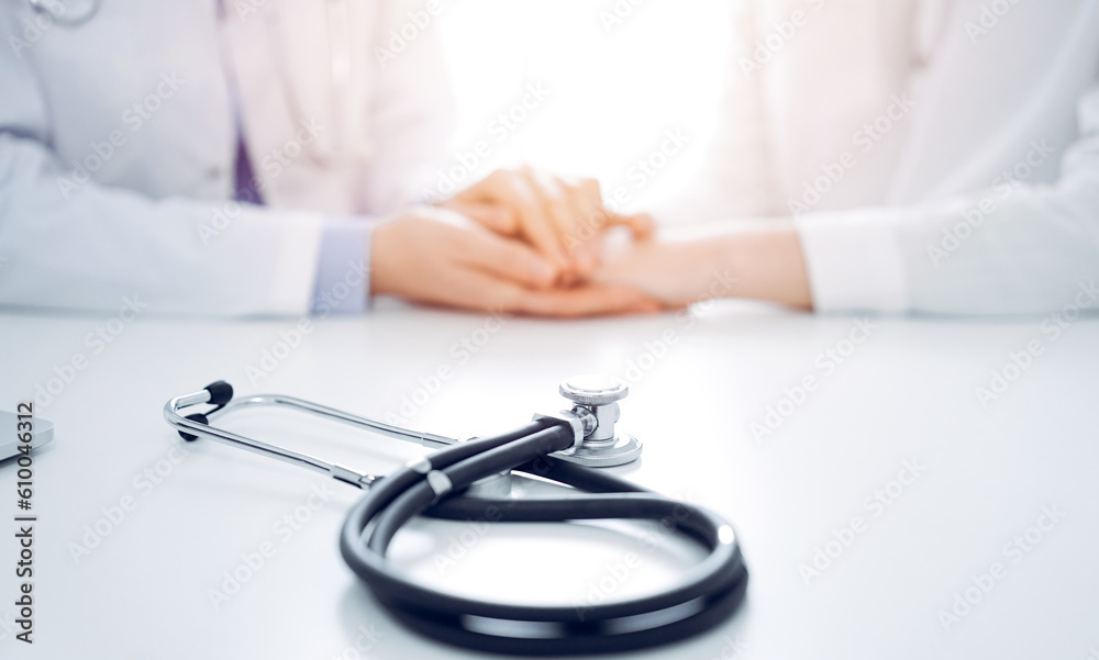 Stethoscope lying on the tablet computer in front of a doctor and patient sitting near each other. Medicine, reassuring hands concept. Stethoscope lying on the tablet computer in front of a doctor and patient sitting near each other. Medicine, reassuring hands concept.