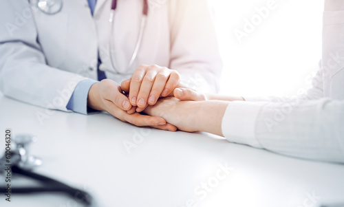 Doctor and patient sitting near each other at the table in clinic office. The focus is on female physician's hands reassuring woman, only hands, close up. Medicine concept.