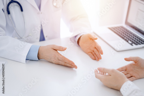 Doctor and patient discussing current health questions while sitting opposite of each other at the table in clinic, just hands closeup. Medicine concept.