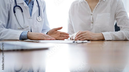 Doctor and patient discussing something while sitting near each other at the wooden desk in clinic. Medicine concept.