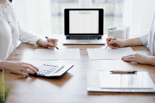 Two accountants using a laptop computer and calculator while counting taxes at wooden desk in office. Teamwork in business audit and finance.