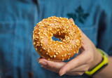 Caramel donut covered with nut sprinkles in hand.  close up. blue background