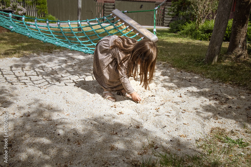 A llittle girl with brown hair plays in the sandbox next to the hammock. photo