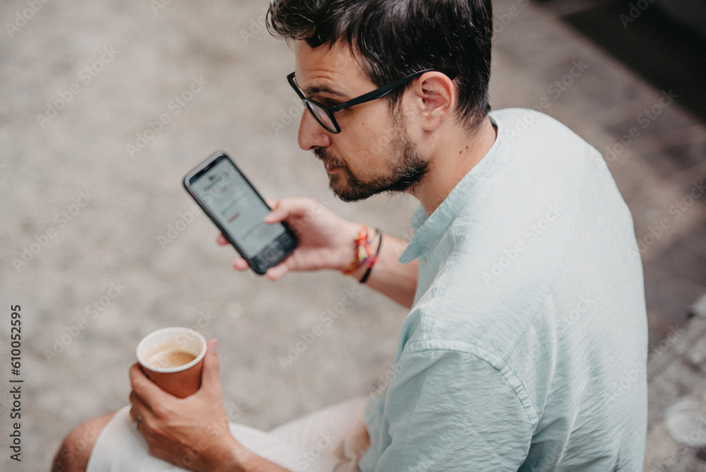 Young man passing the time on his cell phone while holding a cup of coffee. Young man passing the time on his cell phone while holding a cup of coffee.